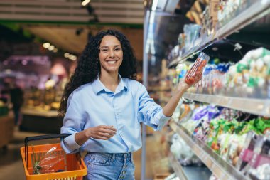 Portrait of beautiful vegetarian woman in supermarket, Latin American woman chooses vegetables for dinner, smiling and looking at camera. clipart