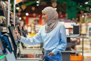 Bir kadın alıcı süpermarkette tesettür içinde mal için ödeme yapar self-servis kasasında, müşteriler için uygun hizmet.