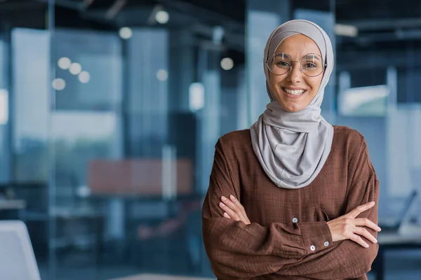 stock image Portrait of successful and happy businesswoman in hijab, office worker smiling and looking at camera with crossed arms, working inside modern office.