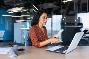 Portre başarılı bir iş kadını, Latin Amerikalı kadın bir ofis binası içinde online video konferansında çalışan, laptop ekranındaki interlocutors 'un finansal belgelerini gösteriyor..