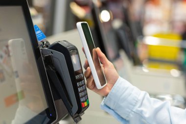 Kapalı gişe Kadın Tezgâhı Elektronik Ödeme Süpermarket akıllı telefonu satın aldı. Cep telefonlu bir kadın mağazalardan satın almak için ödeme yapıyor. NFC Sınırsız Terminal Kapatma Kart Okuyucu Okuyucusu.