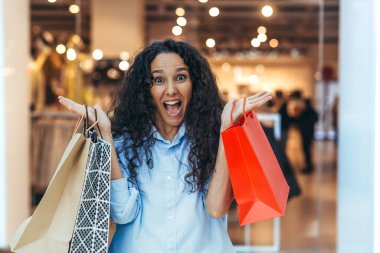 Genç, güzel bir İspanyol, Latin Amerikalı kadın indirimli indirimlerle bir süpermarketten alışveriş yapıyor. Mutluluk sevinçle haykırır, renkli paketleri mallarla gösterir.