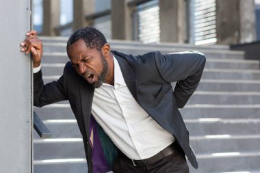 Afrika kökenli Amerikalı bir adam ofis binasının dışında çok çalışıyor. Takım elbiseli bir patronun sırt ağrısı var. Merdivenlerin yakınında el ele tutuşan bir iş adamı..