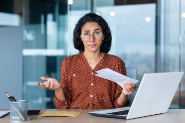 Hayal kırıklığına uğramış iş kadınının portresi, Latin Amerikalı bankadan kötü haberli bir mektup aldı, ofis çalışanı kameraya üzgün bakıyor, bilgisayarını kullanarak çalışıyor..