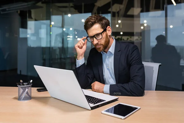 Stock image Serious thinking senior businessman working inside office using laptop, man in glasses solving problem, mature investor in business suit.