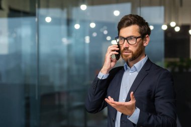 Ciddi ve başarılı bir iş adamı pencerenin yanında telefonla konuşuyor, takım elbiseli ve sakallı bir adam..