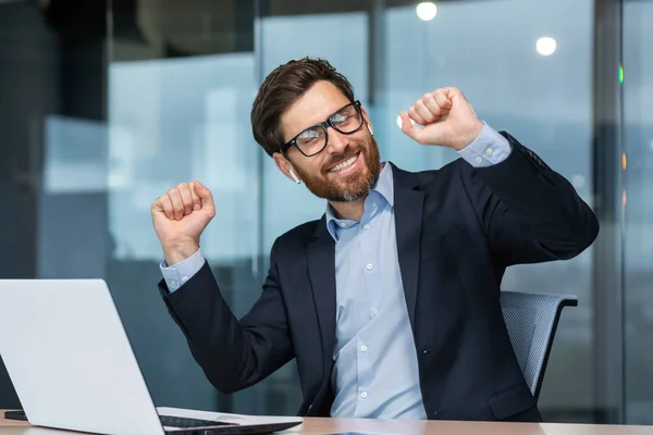 stock image Mature businessman in office dancing sitting at desk, senior man working inside building celebrating successful achievement with laptop.