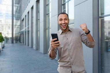 Genç, yakışıklı İspanyol bir adam, elinde telefon tutan Afrikalı bir Amerikalı, online oyunlar oynuyor, eliyle evet diyor. Kameraya bakıyor, zafere seviniyor, ben kazanacağım..