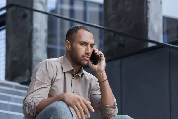 一个严肃而震惊的非洲裔美国人的画像 他闷闷不乐地坐在外面的台阶上 伤心地在电话里说着话 把目光移开 — 图库照片
