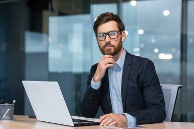 Olgun, ciddi düşünen bir iş adamı ofis içinde çalışıyor, iş elbisesinin baş yatırımcısı laptopta beyin fırtınası stratejisi ve plan üzerinde çalışıyor..