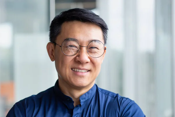 stock image Close up photo portrait of successful and happy Asian businessman, mature boss with glasses working inside modern office building senior investor smiling and looking at camera