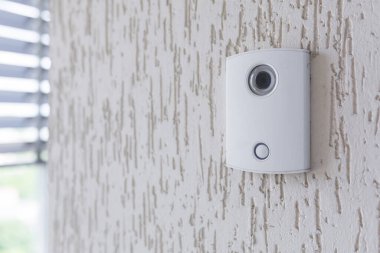 Beyaz bir elektronik kapı zili. Binanın duvarında bir kamera var..
