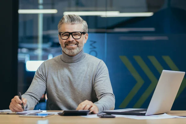 Stock image Portrait of successful senior businessman, gray haired man in glasses smiling and looking at camera, mature investor boss working inside modern office building using laptop at work.