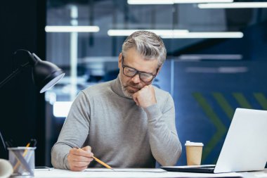 Ciddi düşünen mimar tasarımcı planlar üzerinde çalışıyor. Ofis mühendisi olarak çalışan olgun bir adam..