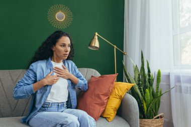 Panik atak geçiren kadın evde yalnız başına. Korkmuş İspanyol kadın. Oturma odasında kanepede otururken nefes almakta zorlanıyor..