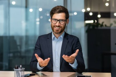 Ofiste oturan, kulaklık takan ve kamerayla konuşan yakışıklı bir adamın portresi. İş toplantısı, özel ders desteği, iş görüşmesi, danışma.