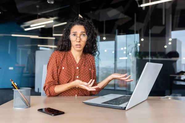 Frustrated and sad woman inside office looking at camera, businesswoman unhappy with achievement results working at desk using laptop at work.