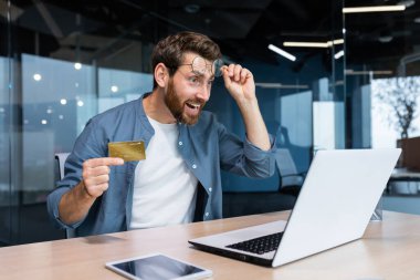 Ofiste çalışan dolandırılmış ve hayal kırıklığına uğramış bir işadamı, elinde banka kartı olan bir adam ve çevrimiçi mağazadan satın almaya çalışan bir adam, online dolandırıcılık ve aldatmaca..