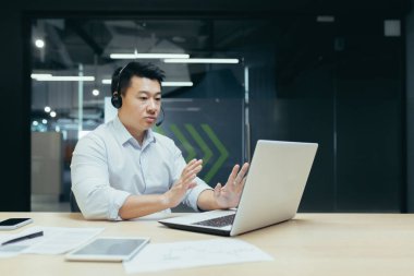 Çevrimiçi satış. Tele-pazarlamacı. Genç bir Asyalı satıcı ofiste bir dizüstü bilgisayarın önündeki masada kulaklıkla oturuyor. Mal satar, siparişleri kabul eder, tavsiyeler, müşteri destek hattı.