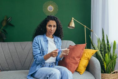 Evdeki bir kadının portresi. Kıvırcık saçlı mutsuz bir İspanyol kadın. Kameraya bakıyor ve istenmeyen bir hamilelik testi tutuyor..