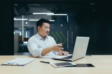 Çevrimiçi iş eğitimi veren kendine güvenen Asyalı genç adam, Webinar. Ofiste dizüstü bilgisayarla oturuyor. Kameraya bakıyor..