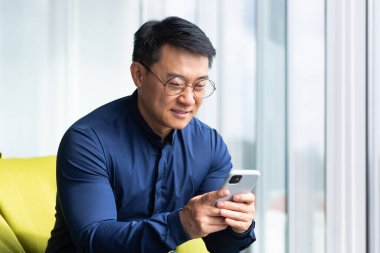 Genç bir adam, Asyalı bir öğrenci, bir ofisin penceresinin yanındaki mindere oturur, çalışma alanı, kampüs. Telefonu elinde tutuyor, bir mesaj çeviriyor, haberleri okuyor, mektupları kontrol ediyor, gülümsüyor..