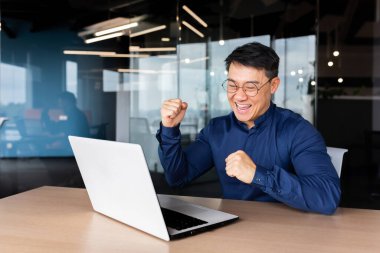 Genç bir Asyalı erkek öğrenci iyi haberler, mektuplar aldı, sınavı geçti, üniversiteye girdi, burs aldı. Ofiste oturuyor, monitöre bakıyor, seviniyor, eliyle evet diyor.