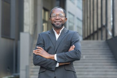 Başarılı Afro-Amerikan patronu kollarını kavuşturup gülümsüyor ve ofis binasının dışında olgun bir adama bakıyor..