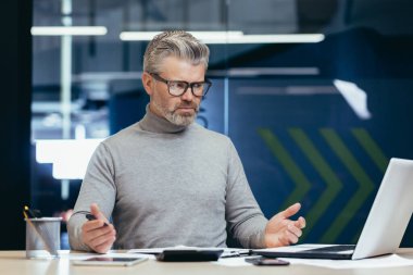 Memnuniyetsiz gri saçlı patron, kıdemli adam başarı konusunda hayal kırıklığına uğradı, olgun iş adamı üzgün ve üzgün, belgelerle çalışıyor ve bina içinde dizüstü bilgisayar kullanıyor..