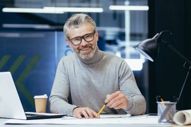 Kıdemli mimarın portresi, gri saçlı tasarımcı gülümseyen ve kameraya bakan adam, planı hazırlıyor stüdyo ofisinde dizüstü bilgisayar ve tablet bilgisayar kullanıyor..