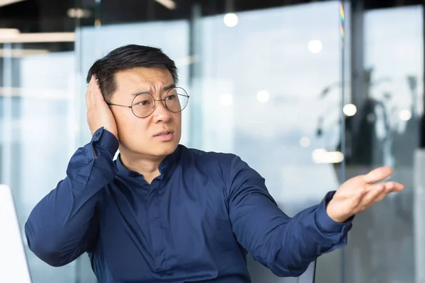 Excessive noise in the office, a businessman tries to be quiet, a man tries to concentrate on work, is disturbed by colleagues in the office, an Asian uses a laptop at work, nervous and angry.