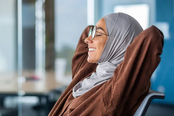 Business woman in hijab resting, Arab woman in hijab with her hands behind her head and smiling with closed eyes, woman in glasses dreaming about future results, good achievements and success.