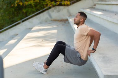 Young african american male athlete doing exercises in stadium on concrete stairs. Squats, shakes hands.