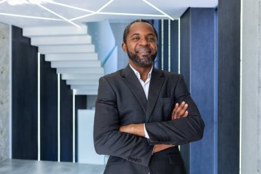 Portrait of successful african american boss, businessman in business suit smiling and looking at camera with crossed arms inside office, man satisfied with work and achievements.
