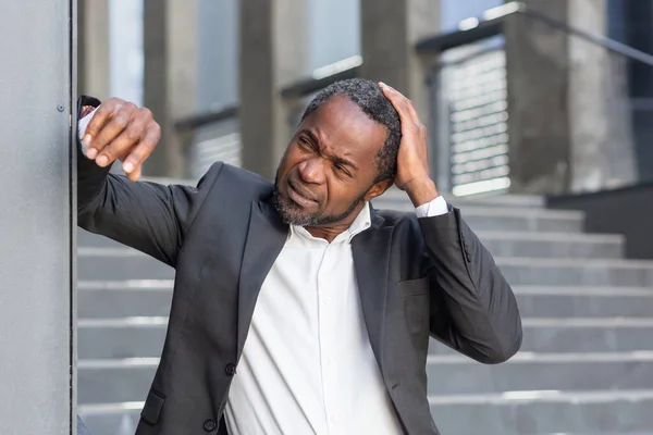 スーツ姿のアフリカ系アメリカ人の高齢者がオフィスの外に立ち 手で壁にもたれかかり 心配そうに頭を上げている 仕事上の問題 — ストック写真