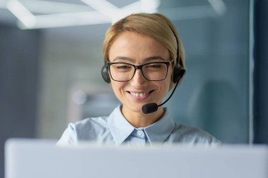 Young female office worker close up, businesswoman with headset phone for video call talking to client remotely, customer support tech worker talking and consulting, successful woman at work.