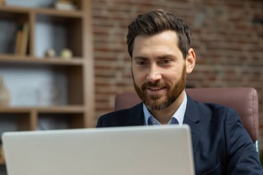 Bilgisayarda çalışan başarılı gülümseyen iş adamının yakın plan fotoğrafı. İnternetteki toplantıda iş kıyafetleriyle uzaktan çalışan meslektaşlarıyla görüntülü konuşma ve gülümseme.