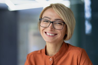 İş yerindeki güzel sarışın iş kadınının yakın plan fotoğrafı. Gözlüklü kadın, gülümsüyor ve kameraya bakıyor. Mutlu kadın portresi..