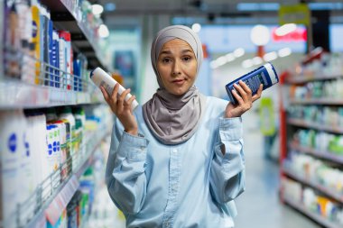 Tesettürlü genç bir Müslüman kadın, ev kimyasalları bölümünde bir süpermarkette duruyor ve elinde iki şampuan tutuyor. Kafası karışık bir şekilde kameraya bakar, seçer, reklamlar, gösteriler.