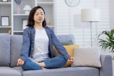 Genç, güzel, Asyalı bir kadın evde tek başına oturuyor. Oturma odasında, Lotus pozisyonunda meditasyon yapıyor. Evde gözleri kapalı oturuyor..