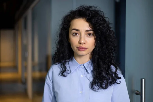 Portrait of a young Muslim woman with curly black hair. Students, businesswomen, freelancers standing in the office and looking at the camera.