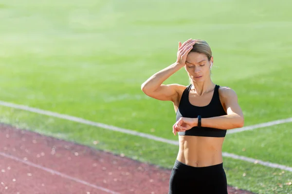 stock image Tired and upset mature female athlete checking heart rate on smart watch fitness bracelet, runner in stadium after active exercise and jogging on sunny day, blonde woman in sportswear.