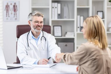 Doktorda tıbbi danışma, hasta doktorların elini zevkle sıkar, beyaz önlüklü olgun bir doktor danışma kliniğinde çalışırken gülümser..