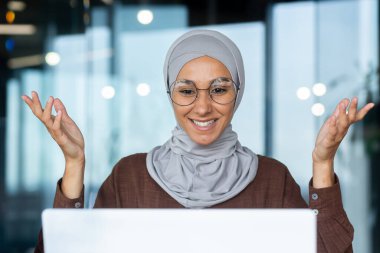 İş yerindeki başarılı ve mutlu kadın tesettürde çalışan işkadını patronu bilgisayarla internetteki toplantıda meslektaşlarına sevinçle el kol hareketi yapıyor.