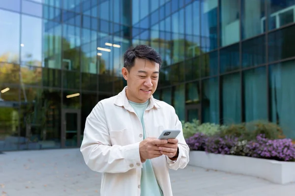 stock image A young male Asian student is standing in a dormitory near the campus and using the phone.