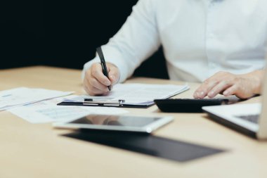 Yakın plan fotoğraf. Bir muhasebeci, denetçi, finansör ve bankacı beyaz bir gömlek teslim ediyor. Ofiste, belgelerle ve dizüstü bilgisayarla çalışıyor. Hesap makinesi kullanıyor..