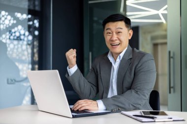 Başarılı Asyalı patronun portresi, başarıyı kutlayan iş adamı takım elbiseli adam gülümseyen ve el ele tutuşan kameraya bakan zafer jesti, ofiste olgun yatırımcı..