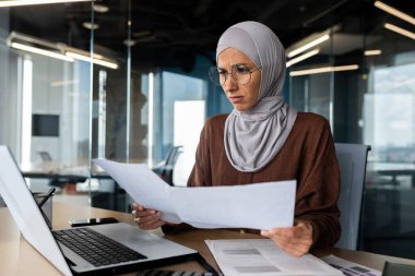 İşteyken yanmış, maddi sorunları var. Kafası karışmış genç başörtülü Müslüman kadın ofiste oturuyor, dizüstü bilgisayarda çalışıyor ve elinde belgeler, grafikler, projeler var..