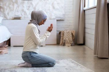 Genç, tesettürlü Müslüman bir kadın dizlerinin üstüne çöküp ellerini kavuşturur, gözlerini kapatır, başını eğip dua eder, yardım ister..