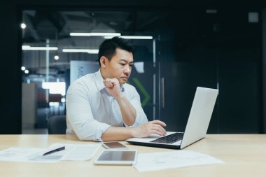 Asya kökenli programcı, ciddi ve düşünceli genç adam, geliştirici dizüstü bilgisayar ofisinde çalışıyor..